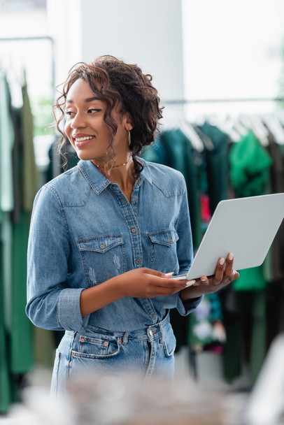 happy african american woman holding laptop in boutique  - Photo, Image