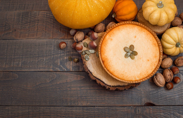 Pumpkin pie on wooden stands surrounded by pumpkins, walnuts and chestnuts on a dark background. - Photo, Image