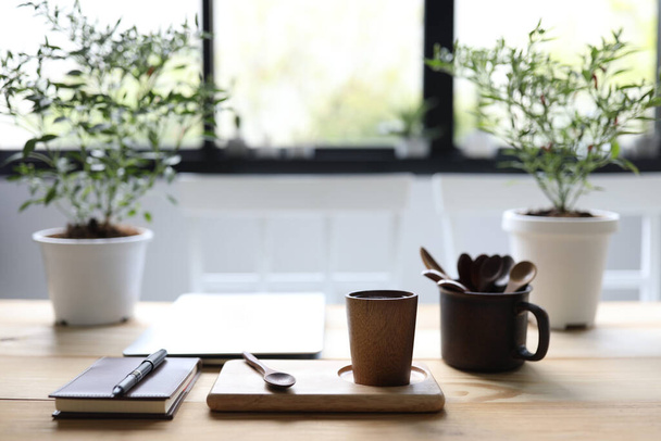 Colher de xícara de madeira e notebook com caneta e vaso de planta na mesa de madeira marrom - Foto, Imagem