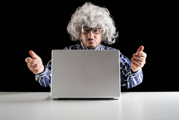 Un adulto mayor desconcertado, boomer típico, no entiende cómo utilizar el ordenador portátil sobre fondo negro - Foto, Imagen
