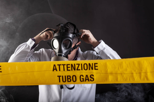 Ένας ιατρικός μηχανικός που φορούσε μάσκα αντιαερίων με εμπειρία στην κρίση διαρροών αερίου κατεύθυνε την κατάσταση έκτακτης ανάγκης κατά τη διάρκεια του χάους. Στην κίτρινη ταινία η γραπτή ειδοποίηση "προσοχή σωλήνα αερίου" - Φωτογραφία, εικόνα