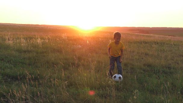 Jongens spelen voetbal op een groen grasveld bij zonsondergang, een voetbalveld, een kind met een bal in de zon, veel plezier met vrienden in een team, gelukkige kinderen, kinderdroom van een voetballer, zonen fantasie - Foto, afbeelding