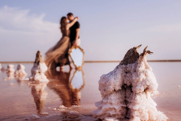 girl and a guy on the shore of a pink salt lake at sunset - Фото, зображення