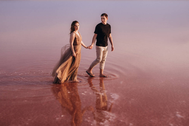 girl and a guy on the shore of a pink salt lake at sunset - Фото, изображение