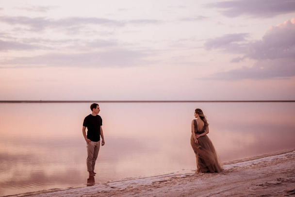 girl and a guy on the shore of a pink salt lake at sunset - Photo, Image