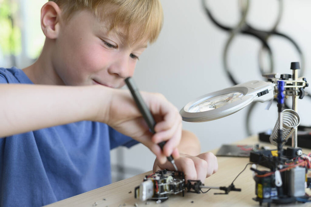 A gyermek átfogó fejlődése. Hobbi a fejlett okos gyerekeknek. Fiatal feltaláló fiú gondosan összeszerelése robot játék csavarhúzóval. - Fotó, kép