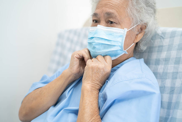アジアの高齢女性高齢者の女性患者は、安全感染を保護するために病院で新しい通常顔マスクを身に着けていますCovid-19コロナウイルス. - 写真・画像