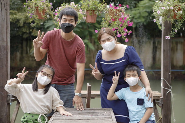ázsiai család visel védelem arc maszk kéz jel győzelem a parkban - Fotó, kép