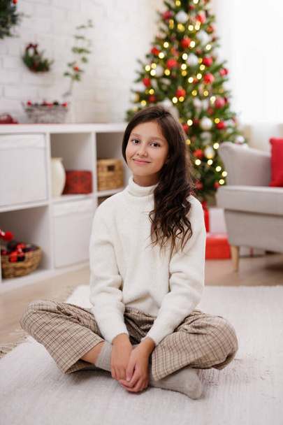 Porträt eines süßen Mädchens im geschmückten Wohnzimmer mit Weihnachtsbaum - Foto, Bild