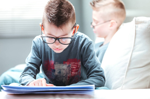 Studierter kleiner Junge mit Brille, der auf einem Sofa liegt und in Großaufnahme von Kopf bis Fuß eine Zeitung in einem Lifestylekonzept liest - Foto, Bild