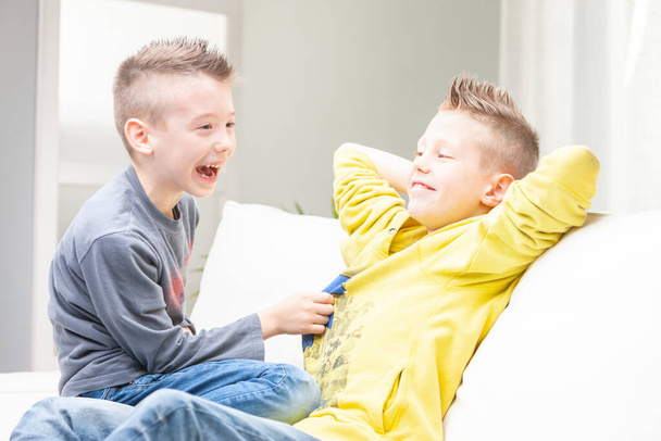 bonito engraçado jovem menino rindo de seu irmão como ele tenta cócegas ele enquanto eles relaxam no sofá juntos em casa - Foto, Imagem