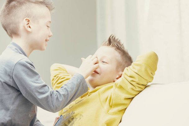 Dois jovens irmãos felizes gostando de brincar juntos dentro de casa em um sofá na sala de estar em um retrato de chave alta de perto - Foto, Imagem
