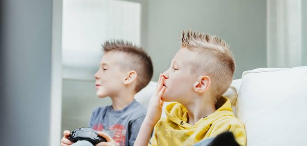 Les jeunes frères qui jouent à des jeux vidéo regardent avec appréhension leurs lèvres en prévision dans un portrait latéral rapproché à l'intérieur à la maison - Photo, image