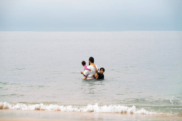 Onnellinen aasialainen perhe, jolla on pieni lapsi pitämässä hauskaa rannalla. Iloinen perhe. Matkustaminen ja loma - Valokuva, kuva