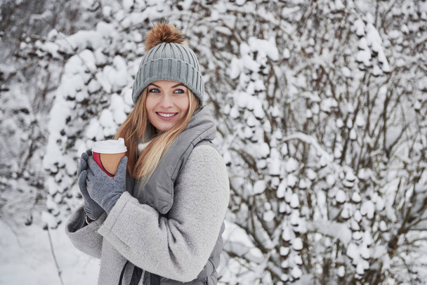 Enjoying the snowy day. Portrait of cute blonde in warm clothes that enjoying spending her weekend outdoors in the winter forest. - Foto, imagen