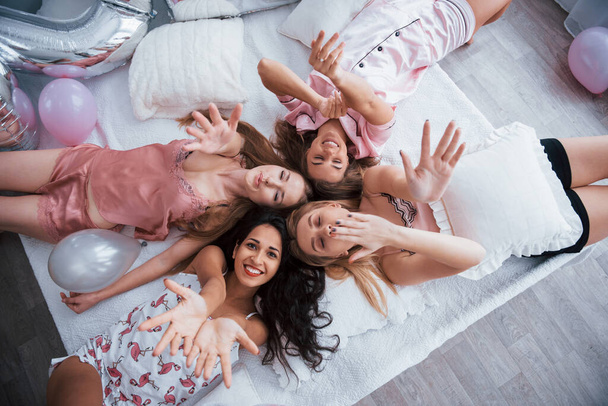 These beautiful friends wish you happy holidays. Top view of young girls at bachelorette party lying on the sofa and raising their hands up. - Foto, Imagem
