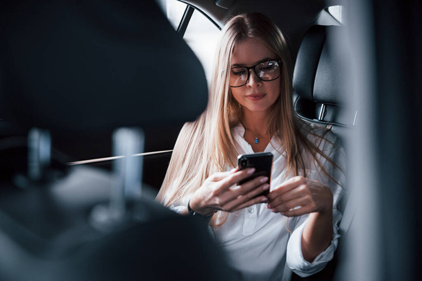 Internet is everywhere. Smart businesswoman sits at backseat of the luxury car with black interior. - Fotografie, Obrázek