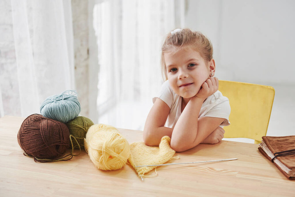 So many threads. Kid is knitting at home. Cute little girl sitting near the wooden table is learning some new stuff. - Foto, Bild