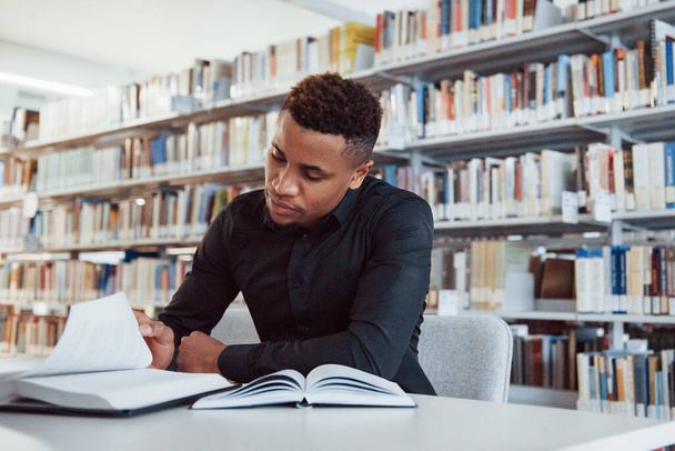 African american man sitting in the library and searching for some information in the books. - Foto, Imagen