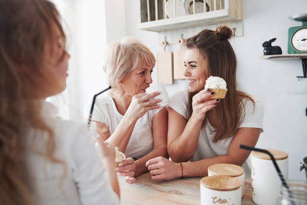 Friendly and calm tea drinking and cake eating. Mother, grandmother and daughter having good time in the kitchen. - 写真・画像