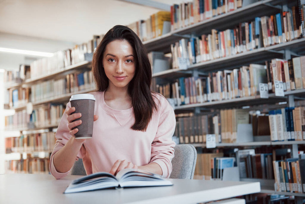 Cute portrait. Brunette girl in casual clothes having good time in the library full of books. - Foto, immagini