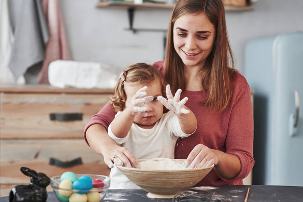 Little girl's hands is in the flour. Mother teaches daughter to paint the eggs for the Easter holidays. - Valokuva, kuva