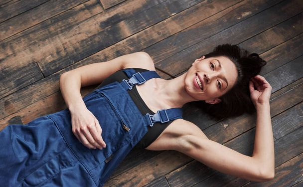Girl in the blue uniform for the work is lying on wooden floor having relax. - Фото, изображение