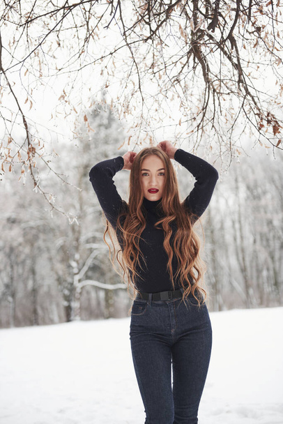 Attractive woman. Pretty girl with long hair and in black blouse is in the winter forest. - Foto, afbeelding