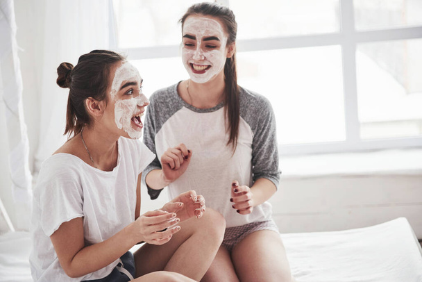 No need spa saloon. Conception of skin care by using white mask on the face. Two female sisters have weekend at bedroom. - Photo, image