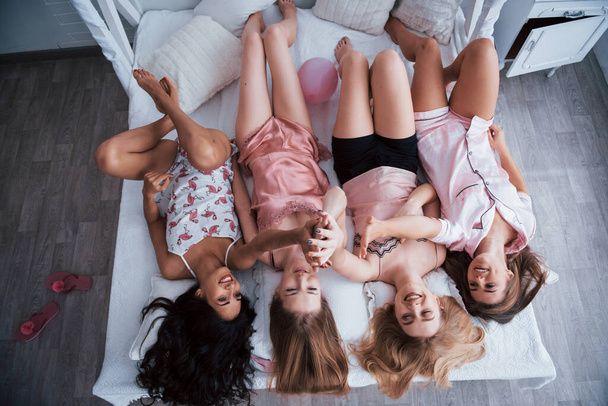 Beautiful hair. Inverted portrait of charming girls that lying on bed in nightwear. Top view. - Foto, Imagem