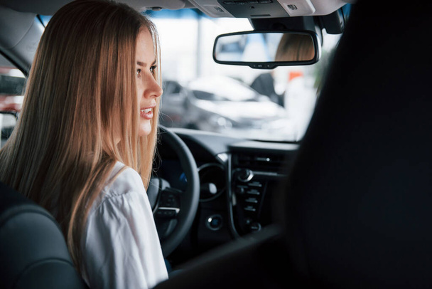 View from behind of the seats. Beautiful blonde girl sitting in the new car with modern black interior. - Fotografie, Obrázek