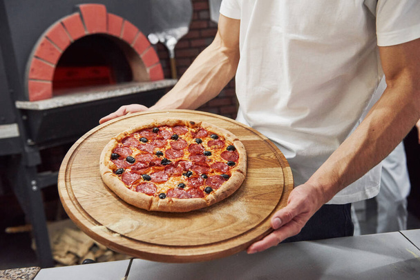 Strong man's hands. Picture of prepared delicious pizza with sausage rings and olives. - Fotó, kép