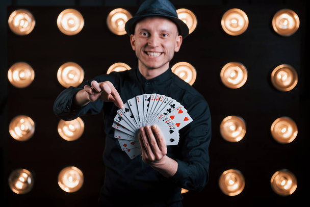 He's takes your card. Magician in black suit standing in the room with special lighting at backstage. - Valokuva, kuva