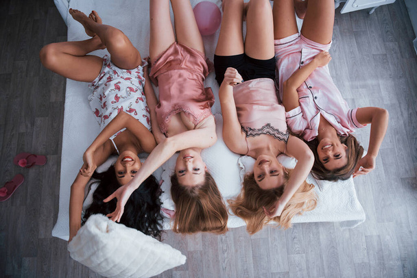 Positive people. Inverted portrait of charming girls that lying on bed in nightwear. Top view. - Foto, Imagem