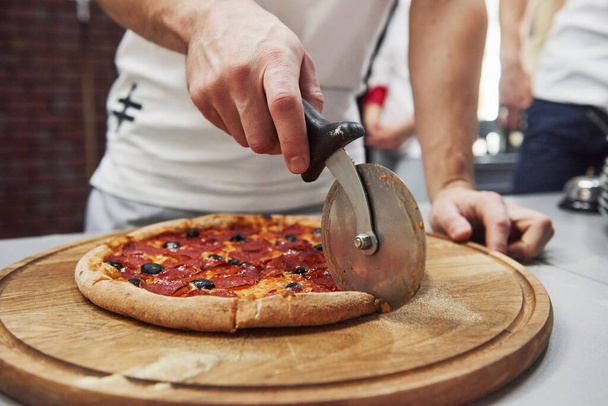 Using special device for cutting. Picture of prepared delicious pizza with sausage rings and olives. - Φωτογραφία, εικόνα