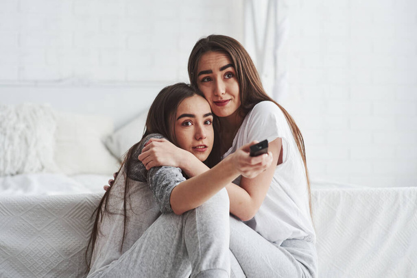 It's so tensing. Sisters have fun watching TV while sits on the floor of beautiful bedroom at daytime. - Fotoğraf, Görsel