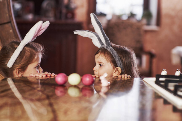 Looks at each other. Funny two sisters in bunny ears looking at each other on the table. - Φωτογραφία, εικόνα
