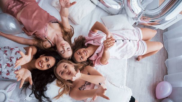 Joy and relaxing. Top view of young girls at bachelorette party lying on the sofa and raising their hands up. - Fotó, kép