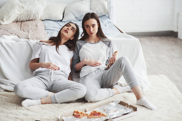 Overeating is never good. Twins have full stomach with pizza. Nice bedroom at daytime. - Φωτογραφία, εικόνα