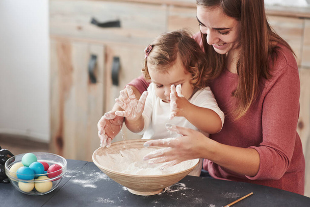 Girl plays with flour. Mother teaches daughter to paint the eggs for the Easter holidays. - Foto, Bild