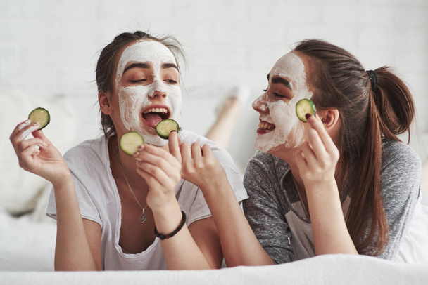 Interesting, how it tastes. Conception of skin care by using fresh cucumber rings and white mask on the face. - Foto, Imagem