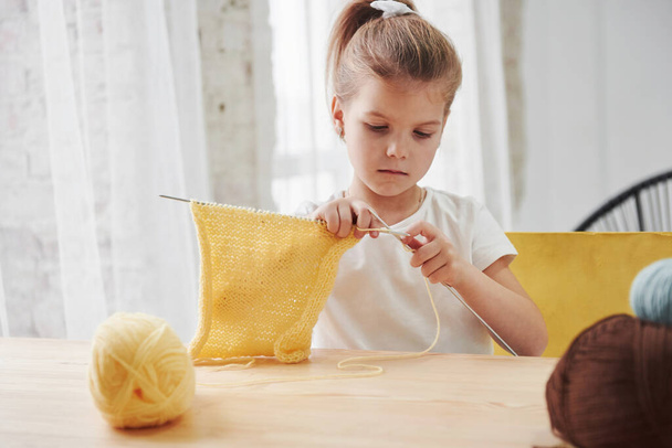 Craft and hobby for a child. Kid is knitting at home. Cute little girl sitting near the wooden table is learning some new stuff. - Φωτογραφία, εικόνα