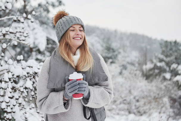 Feeling the satisfaction. Portrait of cute blonde in warm clothes that enjoying spending her weekend outdoors in the winter forest. - Photo, image