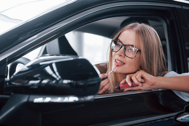 Must to look perfect. Beautiful blonde girl sitting in the new car with modern black interior. - Foto, Imagen