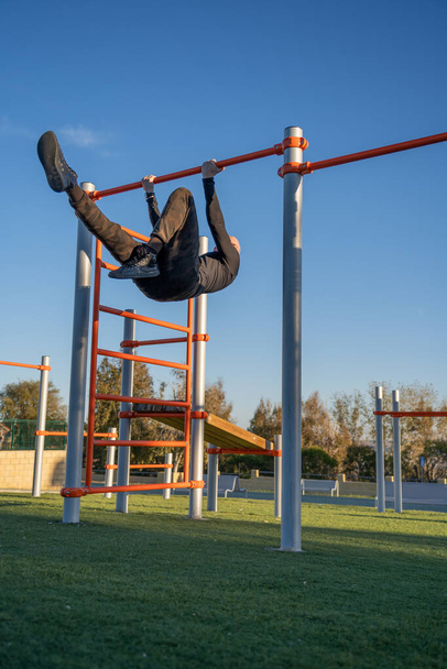 hombre joven y atractivo haciendo deporte en las barras en un parque al aire libre - Φωτογραφία, εικόνα