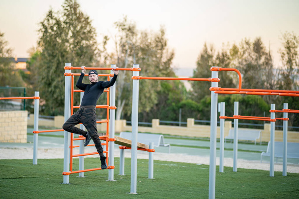 hombre joven y atractivo hacer deporte en las barras en un parque al aire libre - Foto, Imagen