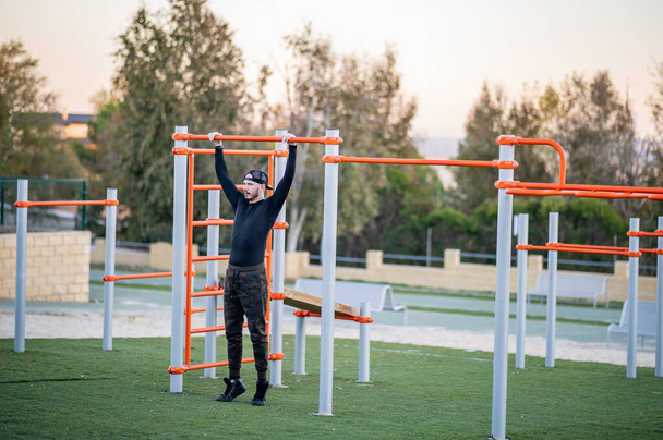 hombre joven y atractivo haciendo deporte en las barras en un parque al aire libre - Photo, Image