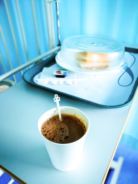 Bebida caliente de chocolate en una taza de poliestireno junto a los alimentos para el desayuno en un hospital. - Foto, imagen