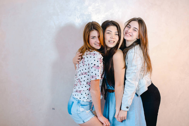 Funny girls pose in camera with smiles on their faces and stand against background of light wall in room. - Photo, Image