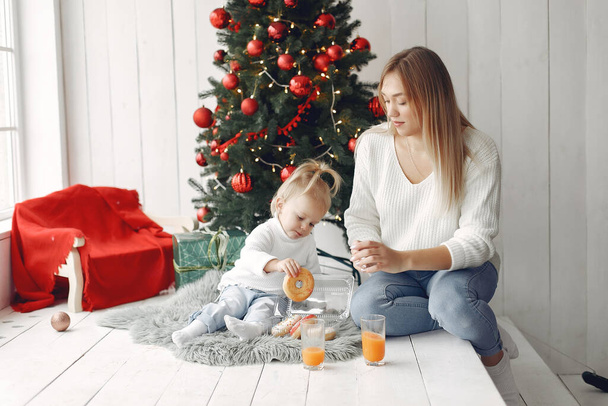 Mother with little daughter sitting near Christmas tree and and go donuts. - Photo, Image